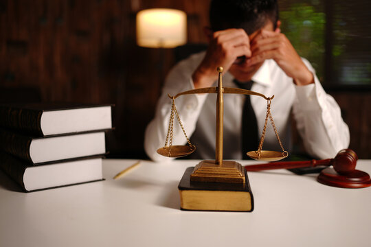 Stressed Lawyer Covering Face at Desk with Scales of Justice and Gavel