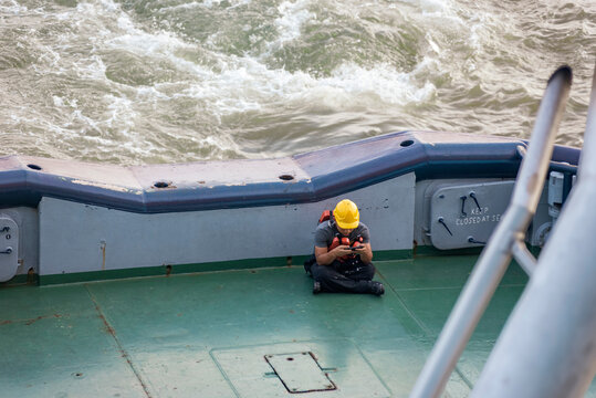 Crew member of a large tugboat relaxing on the stern while using a smartphone during a break at sea.