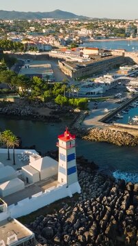 Aerial view of Santa Marta lighthouse and Cascais marina with moored yacht boats with Cascais cityscape, Portugal on sunset. Push in approach dolly move