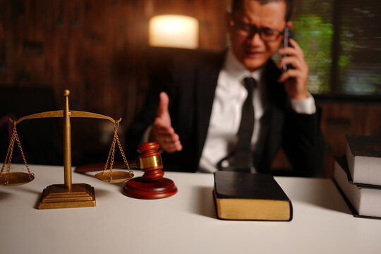 Stressed Lawyer Talking on Smartphone with Scales of Justice and Gavel on Desk