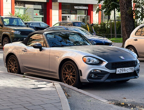 Silver Abarth 124 Spider luxury compact roadster model car parked outdoors. Premium Italian rear-wheel drive RWD sports automobile with matte black hood bonnet and stylish convertible design profile. 