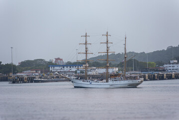 Classic tall ship sailing across calm tropical waters, photographed broadside with its distinctive wooden masts, rigging and white hull against a mountainous coastal landscape. © Mariusz