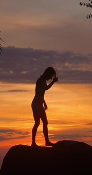 Young Woman Practicing Yoga Silhouetted Against a Warm Orange Sunset