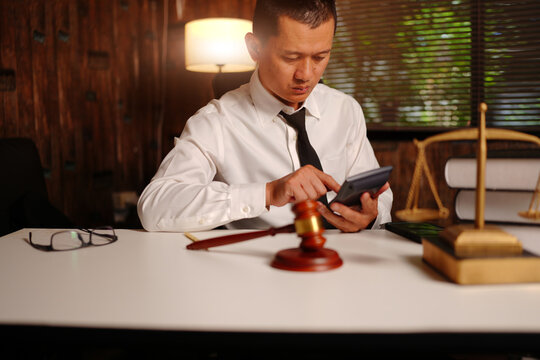 Lawyer Using Calculator with Scales of Justice and Gavel on Desk