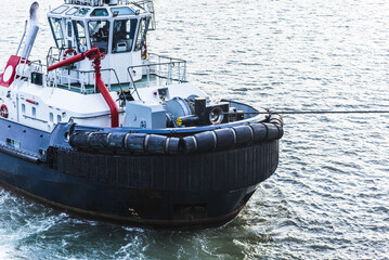 Powerful harbor tugboat assisting a large commercial vessel during port maneuvers, viewed from the front with its robust hull, heavy-duty equipment and wheelhouse clearly visible. © Mariusz