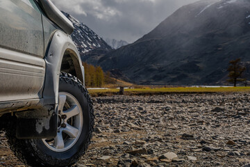 Close up of an off-road 4x4 suv car mud tire parked on a rocky valley bank overlooking scenic mountains, autumn overlanding concept © ANDREY