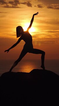 Woman Practicing Yoga Silhouette on Rocky Cliff at Golden Sunset