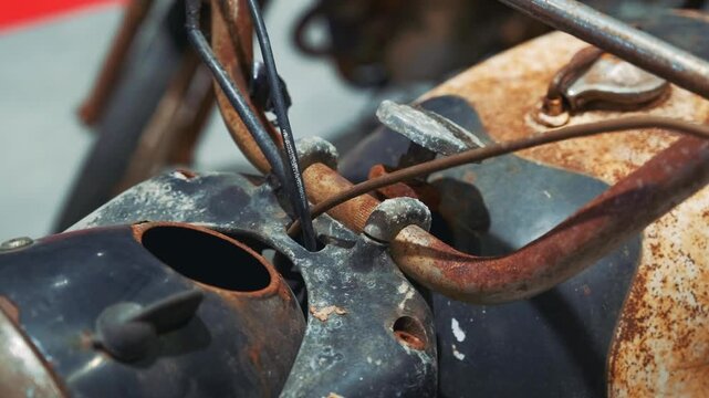 A close-up view of a heavily rusted antique motorbike engine and mechanical parts inside an indoor garage or museum setting, highlighting aged metal components.