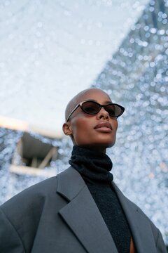 Confident portrait of model in blazer and turtleneck with sunglasses and glittering bokeh backdrop for fashion editorial and banner design