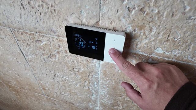 Hand lowering the temperature on a digital heating boiler controller to reduce home energy consumption and heating costs, illustrating smart domestic climate control, conservation, and efficiency.