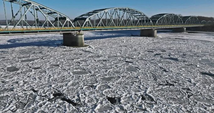 Vehicles crossing a bridge above river covered in ice floes.