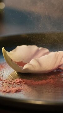 Vertical video: Releasing sifter showering pink powder over white shell on metal plate