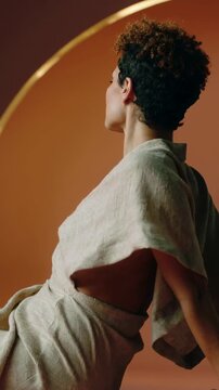 Vertical video: Pressing palms, woman lifting torso on bench in studio, posing in beige linen dress