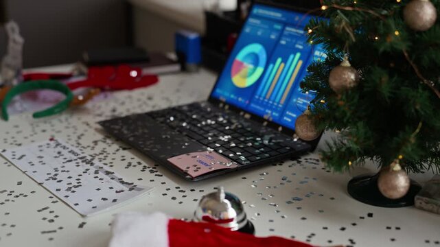 Laptop displaying financial analytics on office desk decorated with Christmas tree and confetti. Footage ideal for corporate holiday campaigns, year end reviews and business presentations