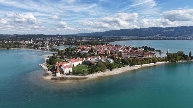 Aerial panoramic view of Lindau Island on Lake Constance in Bavaria, Germany, with the historic old town, marina, waterfront and green Alpine foothills under a dramatic summer sky.