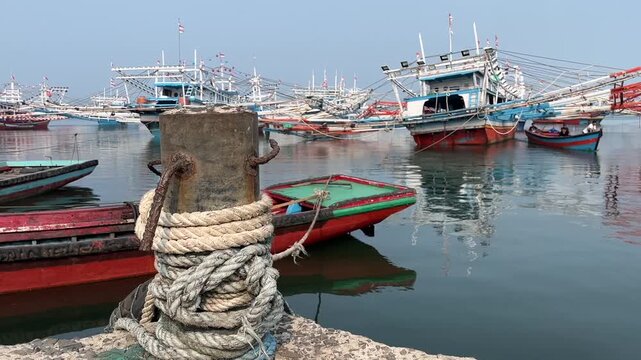 Old rusty bollard wrapped in thick rope at fishing boat harbor