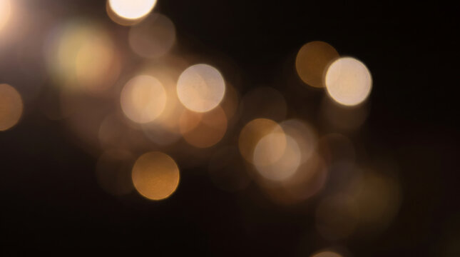 Golden bokeh lights on black background, warm glowing circles, festive abstract light texture