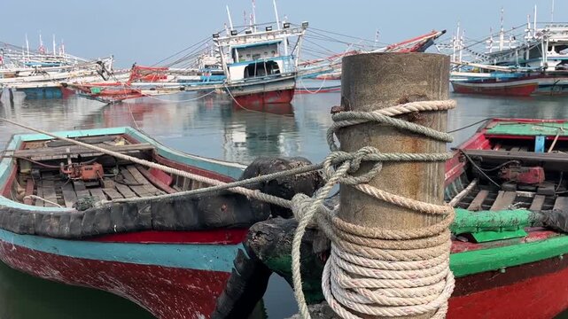 Mooring bollard with tied nautical rope and traditional fishing boats in port