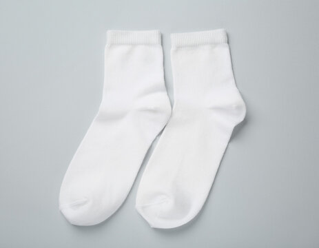 Pair of white socks isolated on a neutral gray background, simple everyday clothing accessory with a clean minimalist appearance.