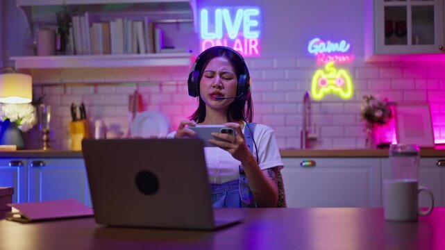 Asian young e-sport woman gamer play online mobile game on smartphone.Attractive girl vlogger influencer content creator gamer enjoy and fun live streaming broadcast games in POV screen and neon room.