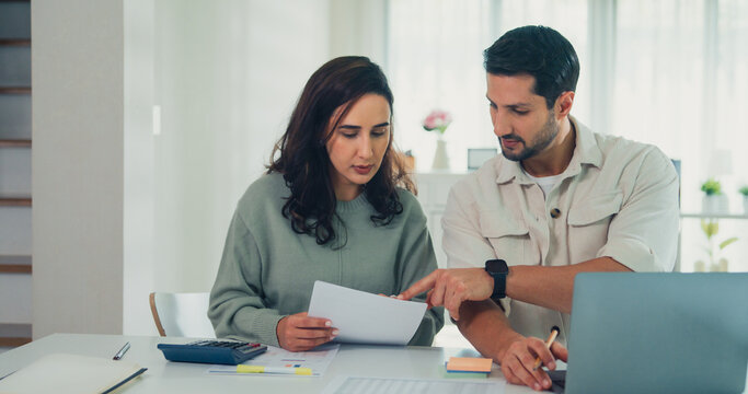 Young Latin couple male, female serious focus on laptop computer check document paper pay bills online plan budget expense in living room at home. Marriage money trouble, Family budget plan concept.