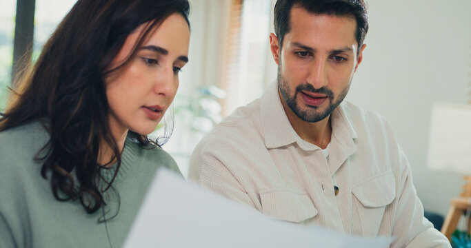 Close up young Latin couple male, female serious focus on laptop computer check document paper pay bills online plan budget expense in living room at home. Marriage money trouble, Family budget plan.