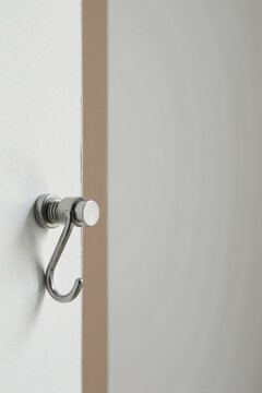 A minimalist metallic hook affixed to a smooth, off-white surface, subtly contrasting against a muted beige backdrop, suggesting a concept of simple elegance and functionality in interior design