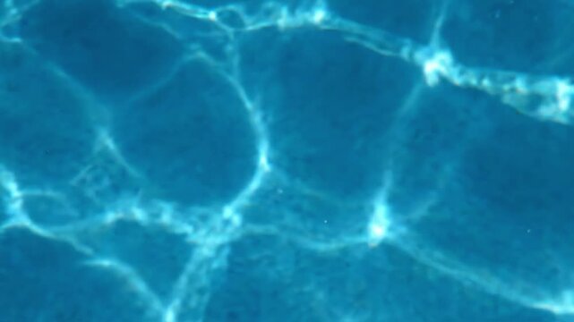 Aqua blue light creates patterns in water in a swimming pool during daytime hours