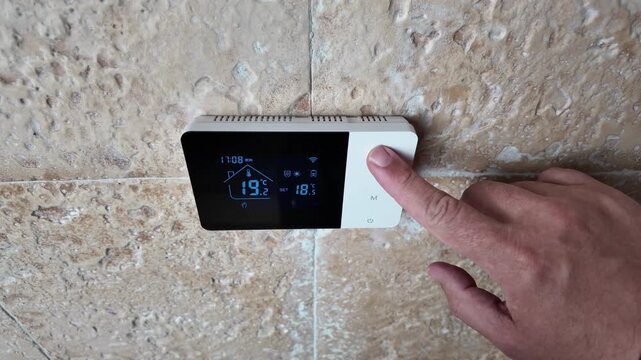 Hand increasing the temperature on a digital heating boiler controller to adjust home indoor climate and energy settings, illustrating domestic heating control, smart thermostatic regulation