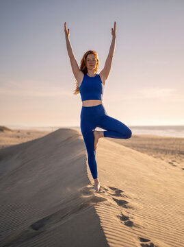 Redhead balances confidently in tree pose atop a sunlit golden sand dune