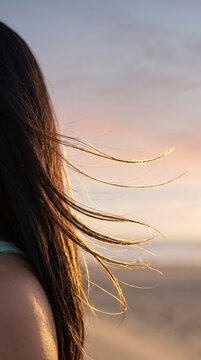 Close detail of windblown hair catching golden light against the sunset sky