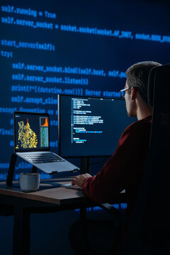 Focused coder works at desk in a dark office with programming code lines running behind. Developer is deeply engaged in a late night data science or AI coding session. Copy space. 