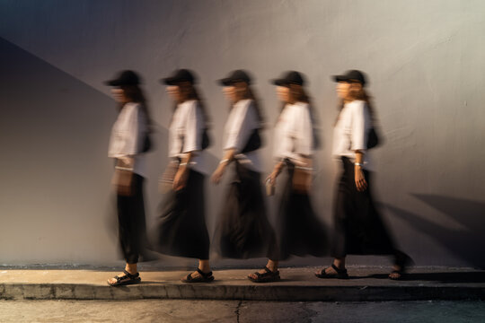 Stroboscopic multiple exposure sequence of woman walking along city wall in warm night light