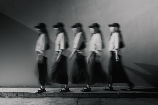 Black and white multiple exposure sequence of Asian woman walking along wall in motion blur