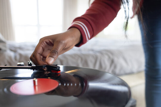 Turntable tonearm is lowering onto spinning black vinyl record on bed near window, reflecting light