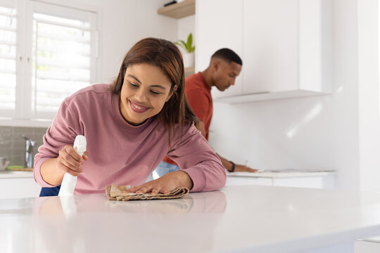 African American couple cleaning white island in modern kitchen using spray bottle and cloth