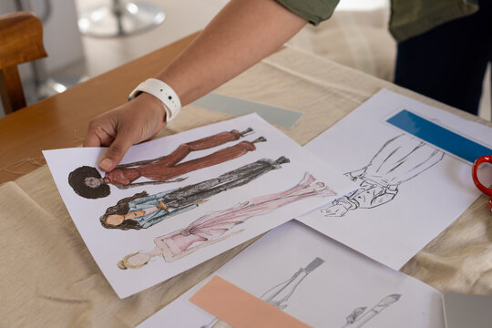 Sheet of fashion sketches occupying center of beige cloth worktable, with scissors and ruler nearby
