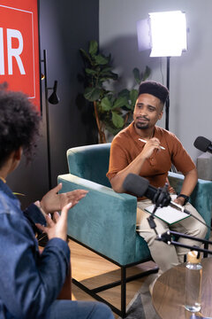 African American man in rust top, woman in denim jacket recording podcast in studio mic, notebook