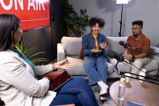 African American host and guests recording podcast on living room set with boom microphones