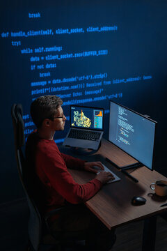 Data scientist works at night on artificial intelligence project, types on keyboard, screens displaying scripts and graphs, projection with running code on a wall behind. Copy space