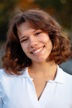 Smiling young woman in white blouse posing outdoors in warm sunlight for a natural lifestyle portrait