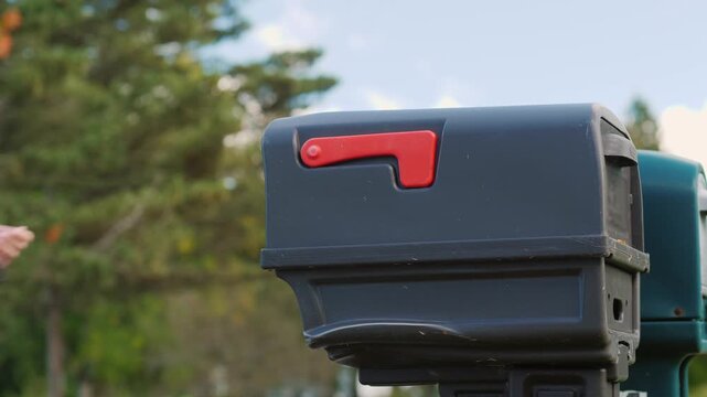 Woman inserts an envelope with letter or greeting card into a black mailbox with red flag up in slow motion.