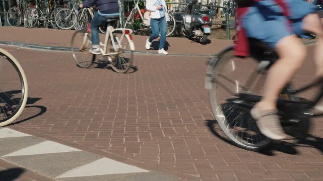 Cyclists riding bicycles on a cobblestone street in a city with parked bikes.