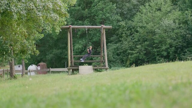 The boy is riding on a zip line swing outdoors