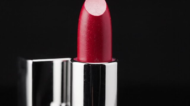 Red lipstick in silver tube close up showing smooth texture and reflective surface against black background
