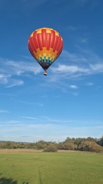 Colorful hot air balloon ascending over green fields on a sunny day