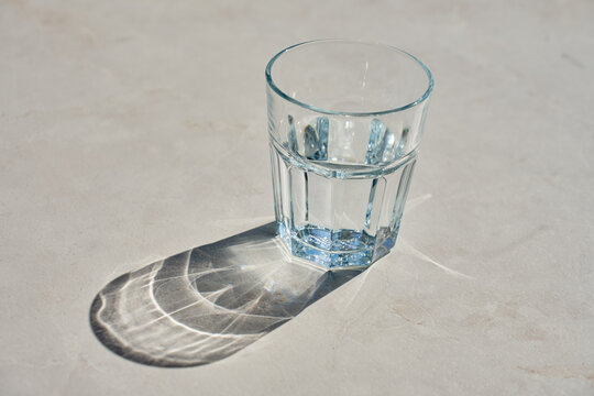 Glass of water in sunlight with reflections and shadows on table