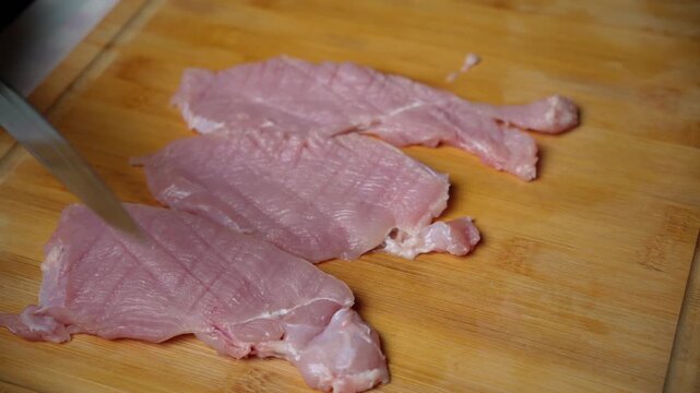 Tenderizing Turkey Steaks Lengthwise. Raw turkey steaks are prepared with lengthwise cuts on a wooden cutting board before seasoning and skillet cooking.