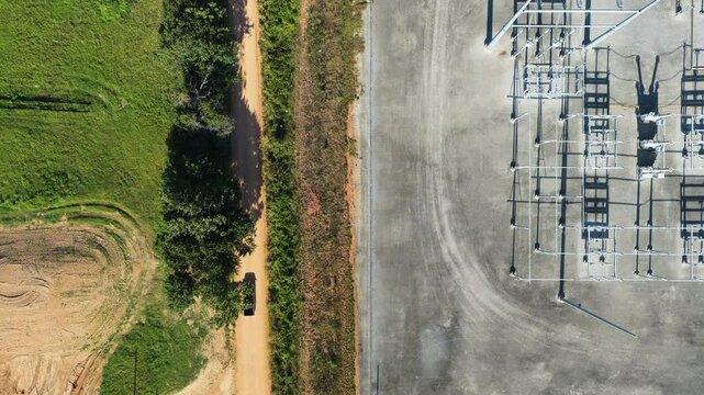 Steel gantries and insulator strings stand on the concrete pad of a substation under construction at Gentry, Arkansas, a dirt access road running along the fence line. Aerial top down flyover