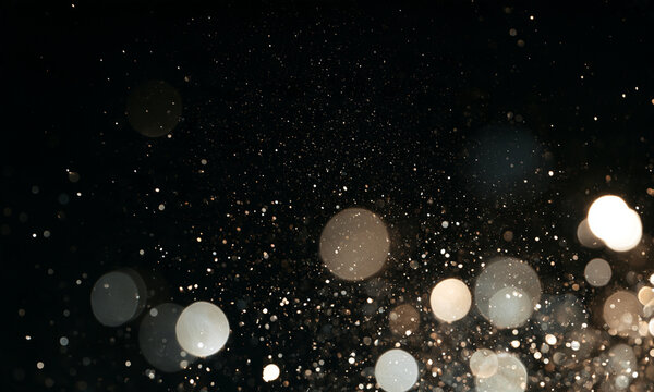 Tiny particles scatter softly against a dark background. The bright bokeh orbs vary in size and opacity with warm and neutral tones. This image is ideal for atmospheric or festive visual.